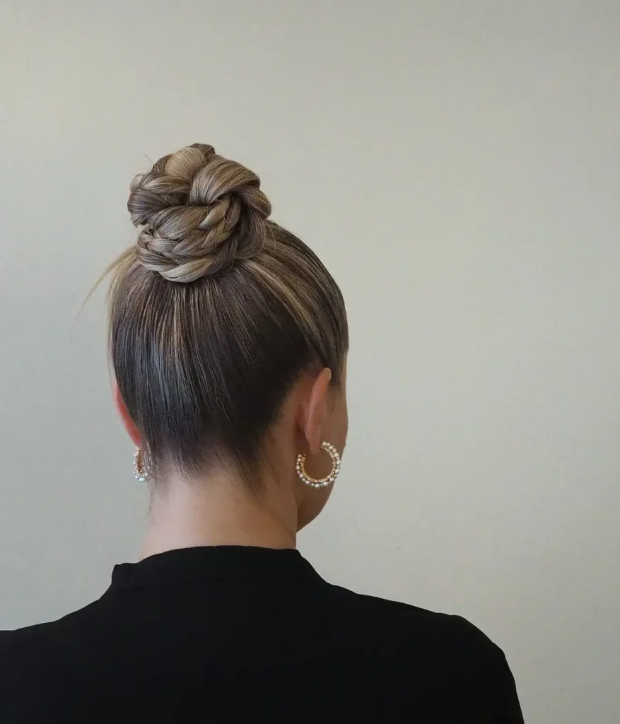 Sleek top knot braided bun with woven braid details and subtle blonde highlights.