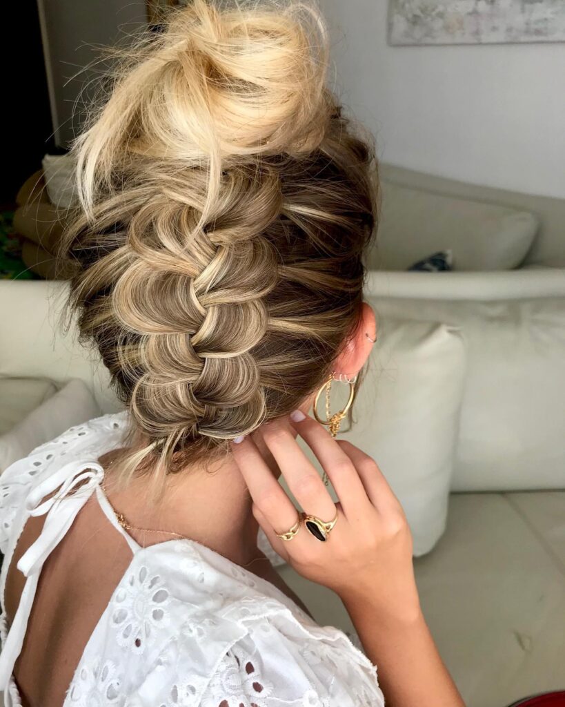 Voluminous blonde braided top knot hairstyle with a loose textured braid.