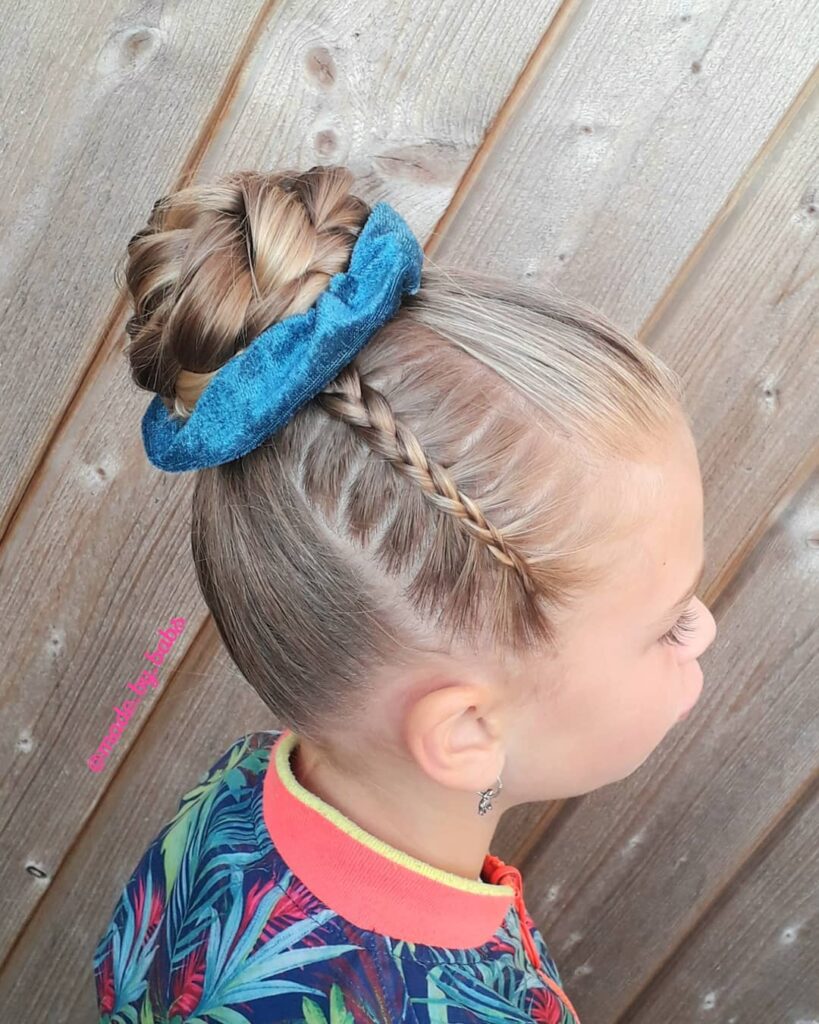 Blonde braided top bun hairstyle with a blue scrunchie and a thin side braid.
