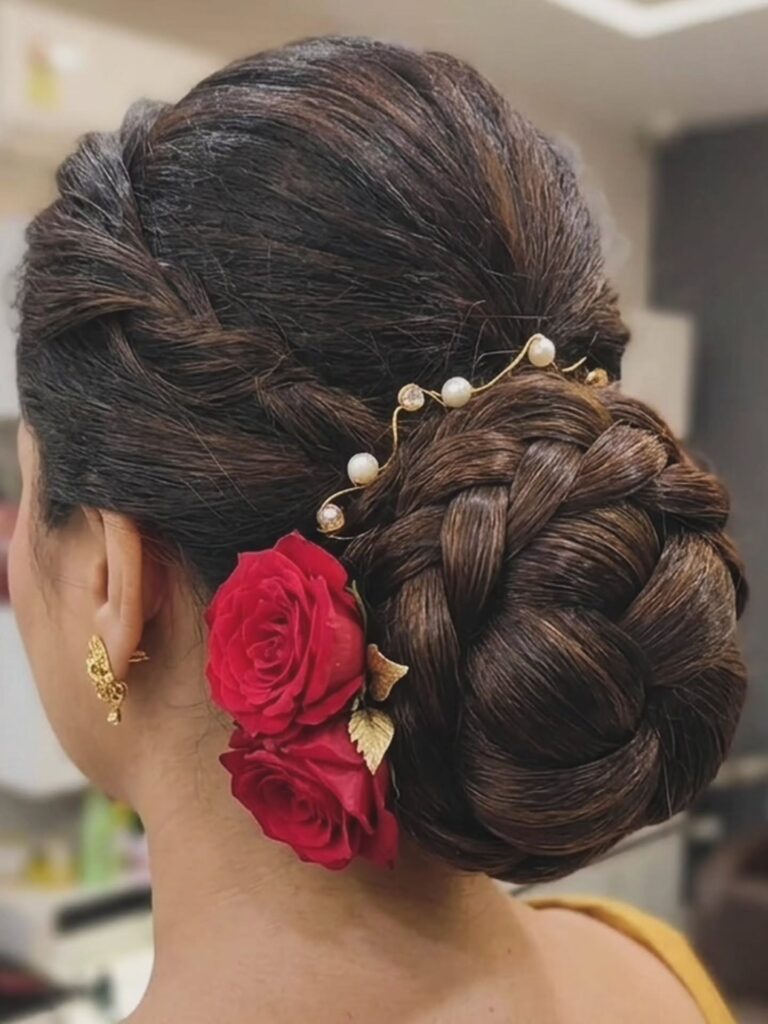 Dark brown braided low bun hairstyle with red roses and pearl hair accessories.