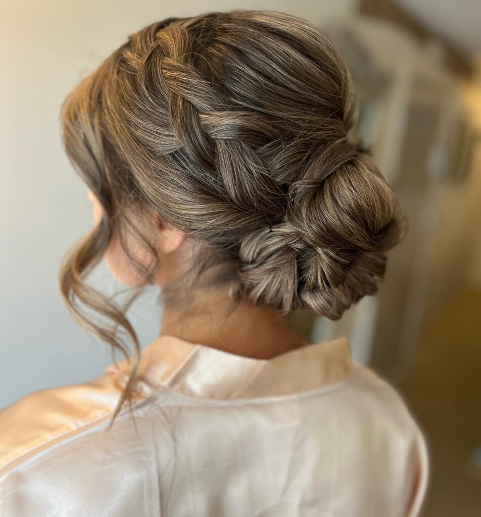 Loose side braided low bun hairstyle with soft curls and warm brunette tones.