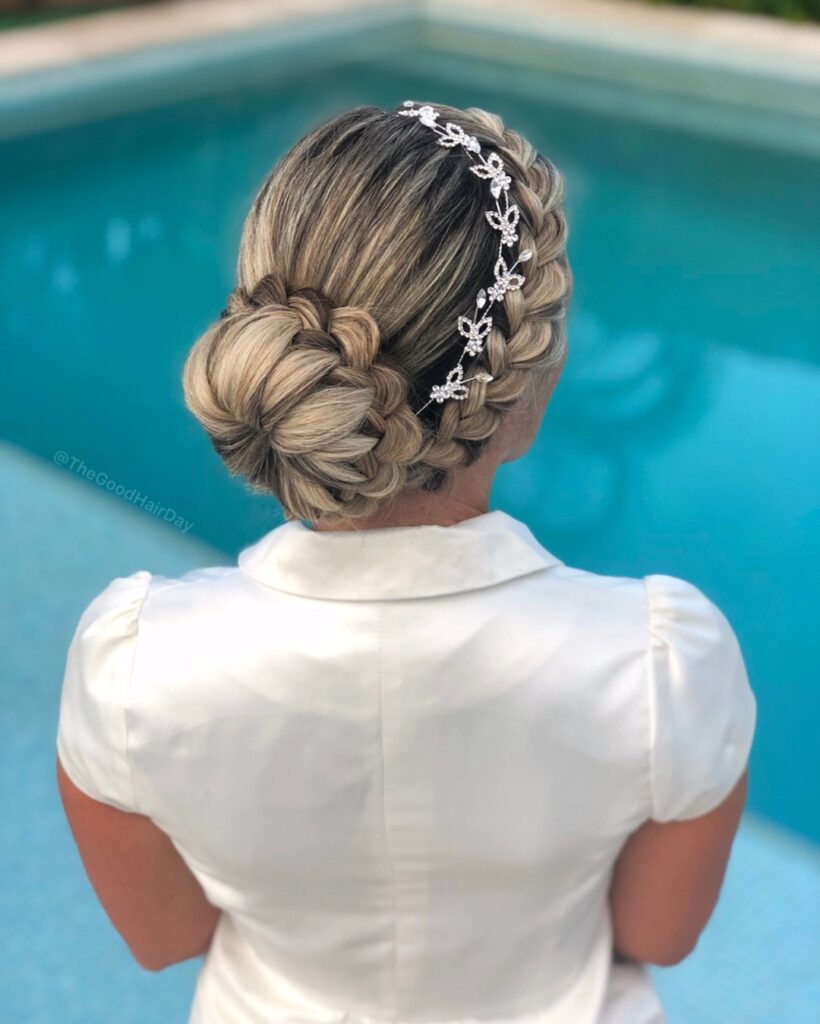 Blonde braided low bun hairstyle with a side braid and decorative bridal hair accessory.