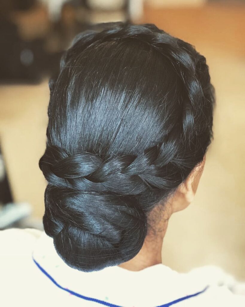 Smooth black low bun hairstyle with a thick side braid wrapped into the bun.