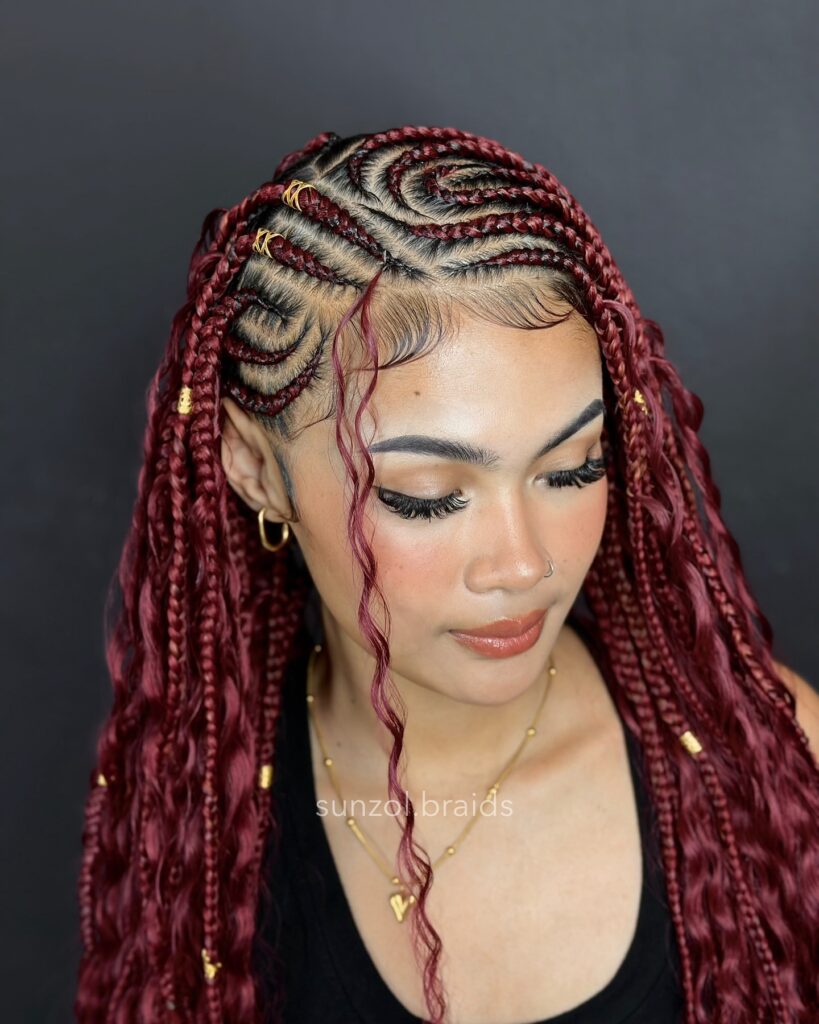 Long burgundy Fulani braids with swirl cornrow patterns and loose curled strands at the front.