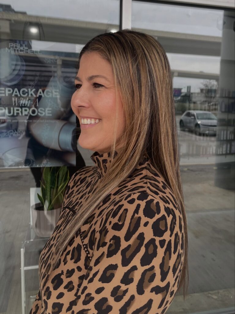 A woman with very long straight brown hair featuring bright caramel highlights throughout.