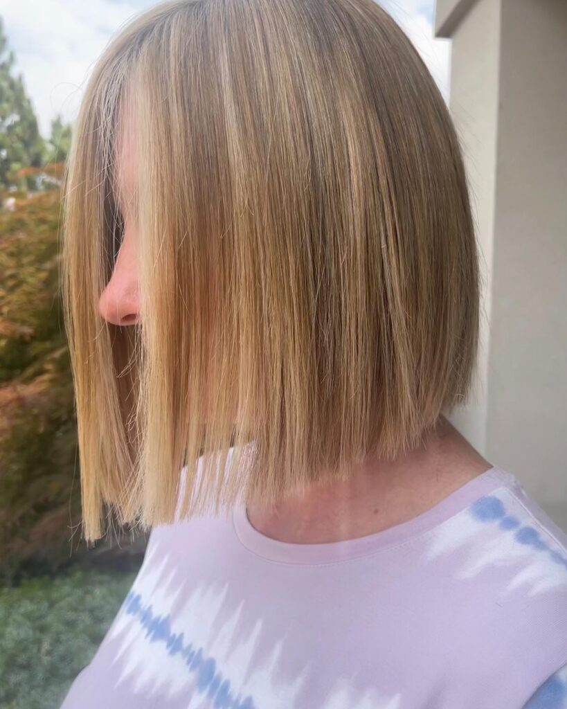 A woman with straight shoulder length blonde hair featuring warm golden highlights and soft layers.