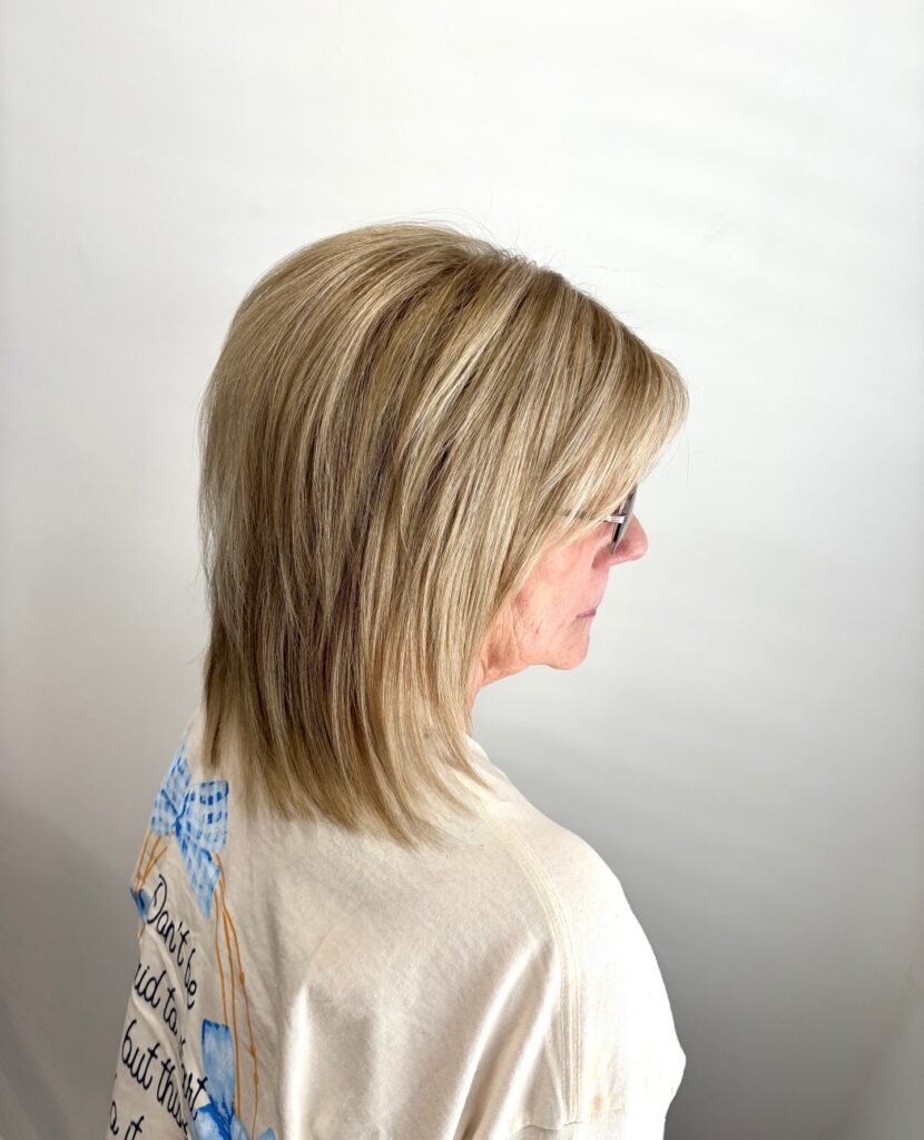 A woman with shoulder length blonde hair styled in a straight layered lob with subtle highlights and side swept bangs.