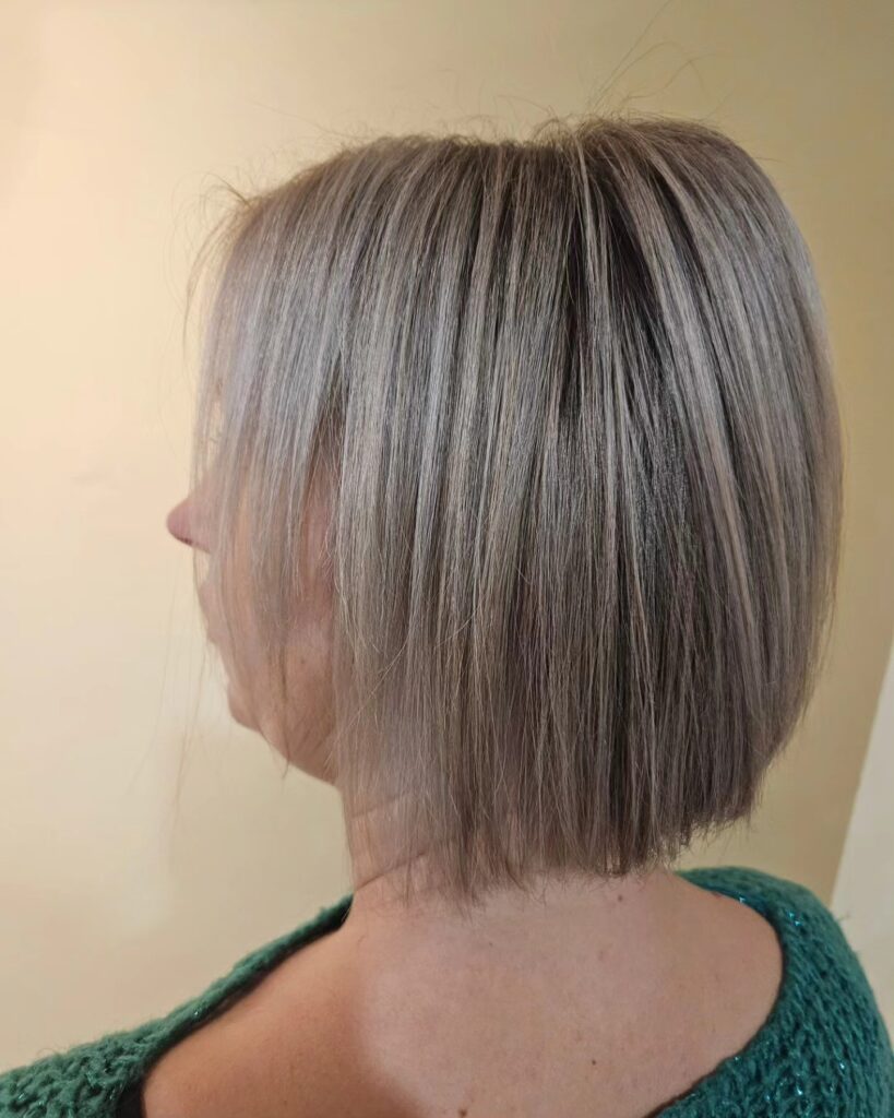 A woman with a short straight silver pixie cut featuring soft side swept bangs and a bright white color.