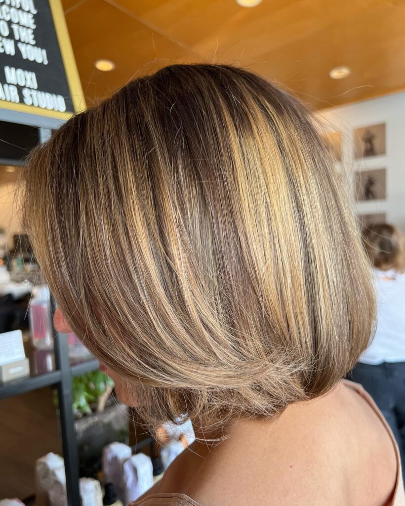A woman with a straight shoulder length chestnut brown bob featuring golden highlights and layered ends.