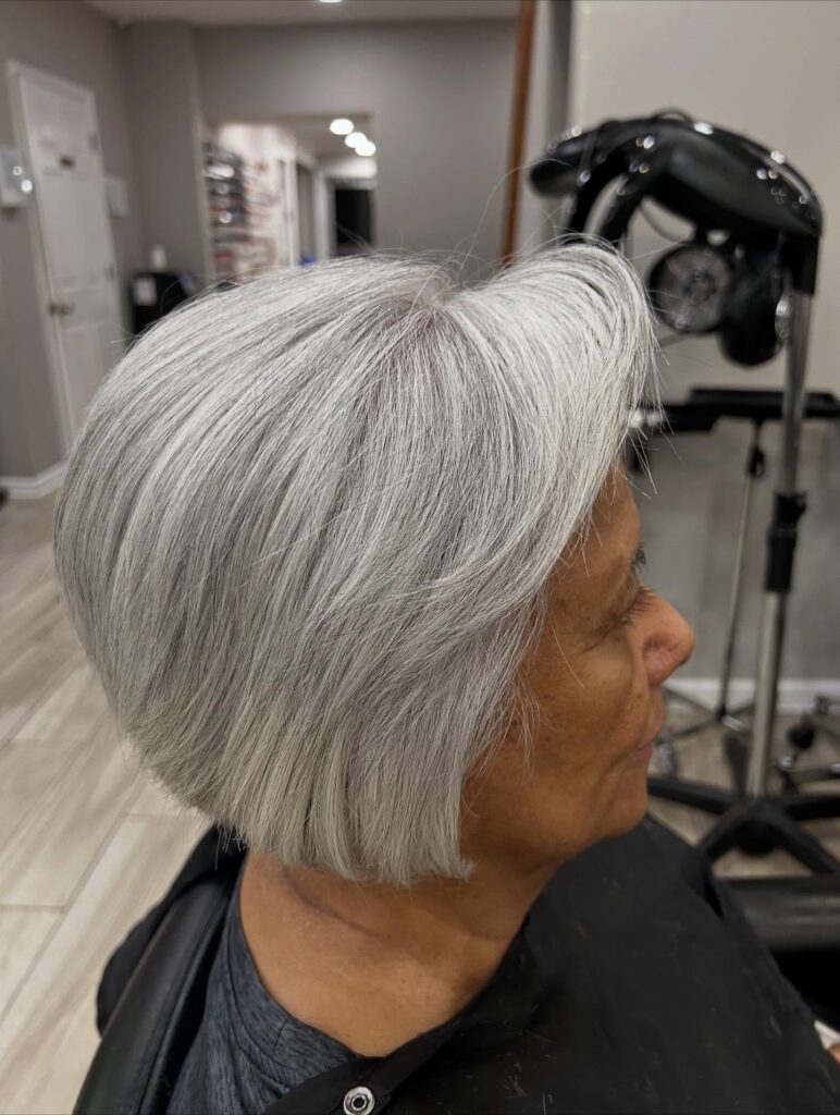 An older woman with a square face wears a voluminous silver bob with a deep side sweep and a rounded back.