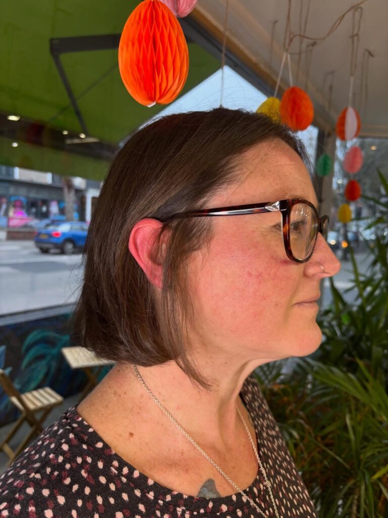 A woman with a square face shape wears a classic chin length brunette bob that is tucked behind her ears.