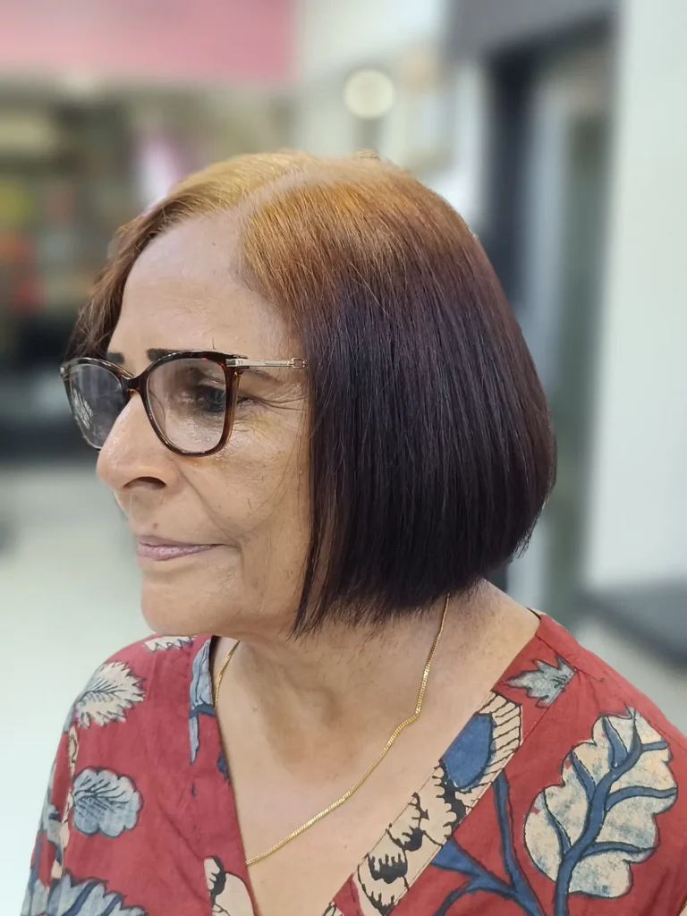 A woman with a square face shape wears a straight chin length bob with a two toned color gradient of copper roots and dark burgundy ends.