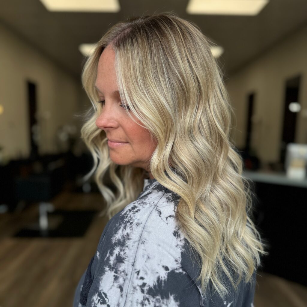 A woman with long honey blonde hair styled in polished mermaid waves that fall over her shoulders.
