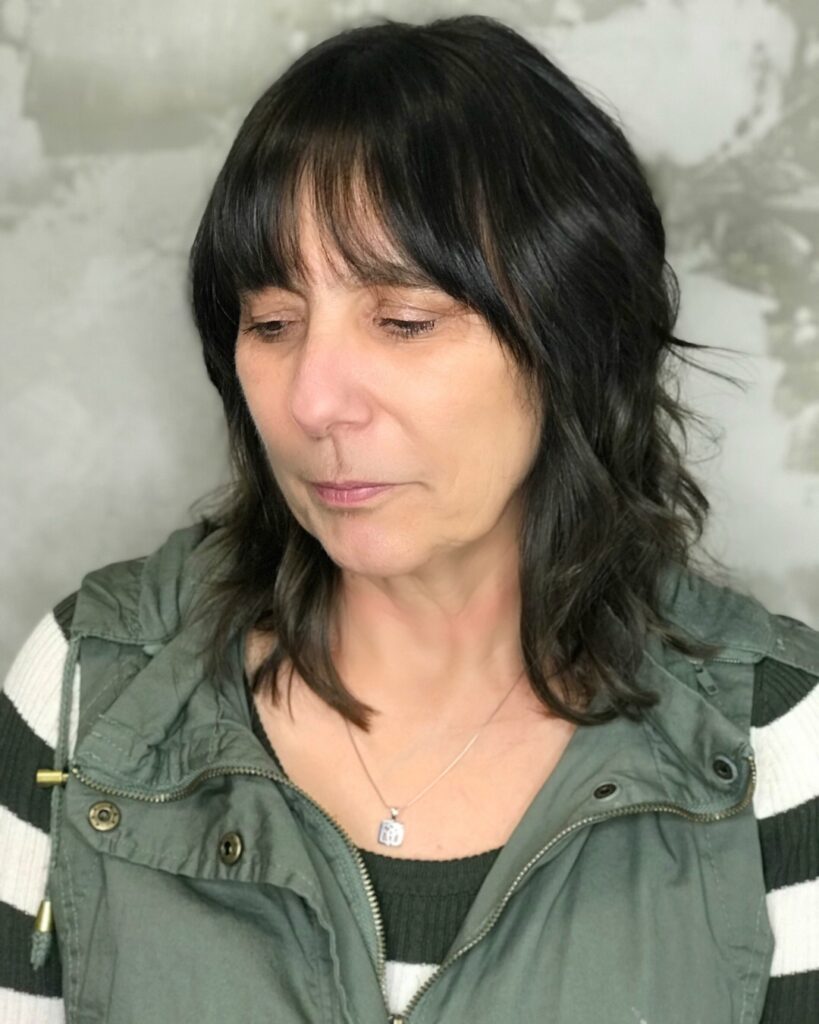 A woman with a dark brunette shoulder length shag haircut featuring a full fringe and textured layers.