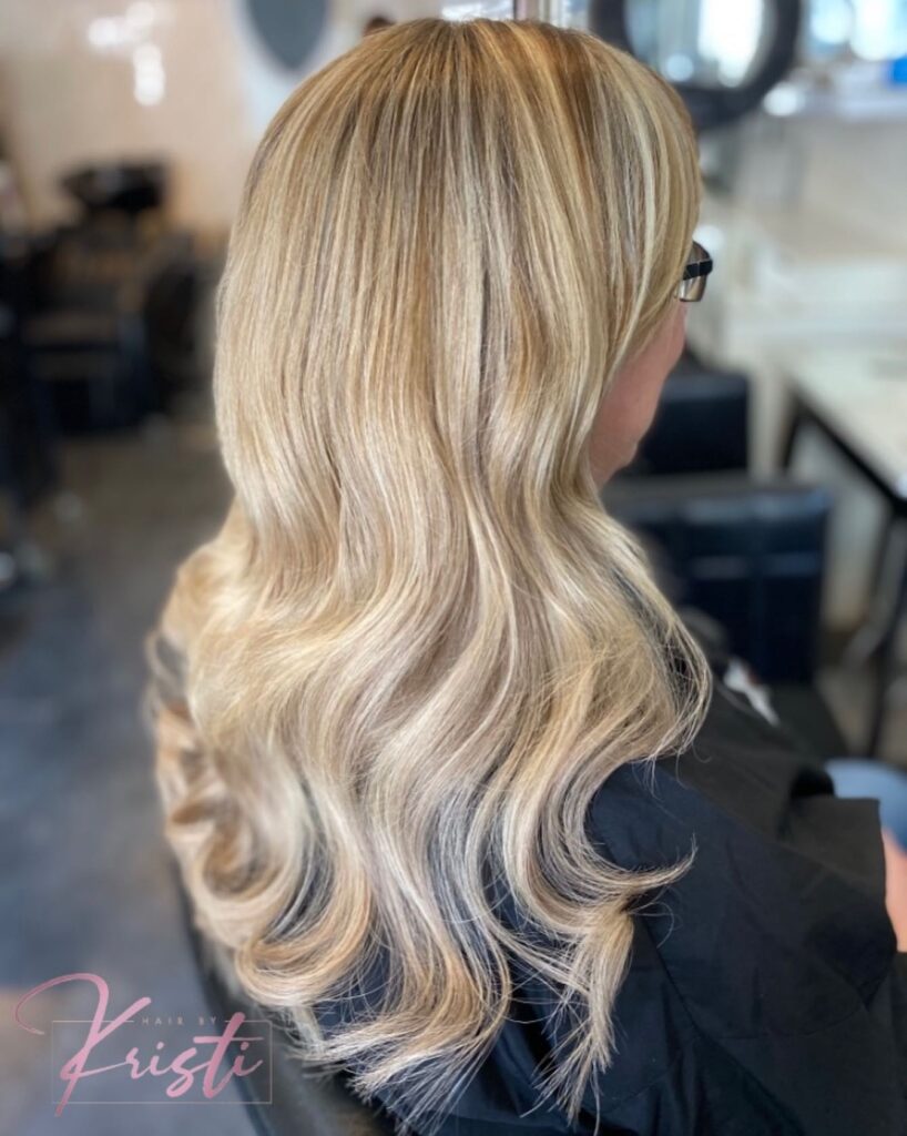 A woman with long fine hair styled in soft voluminous waves with a blend of golden and honey blonde highlights.