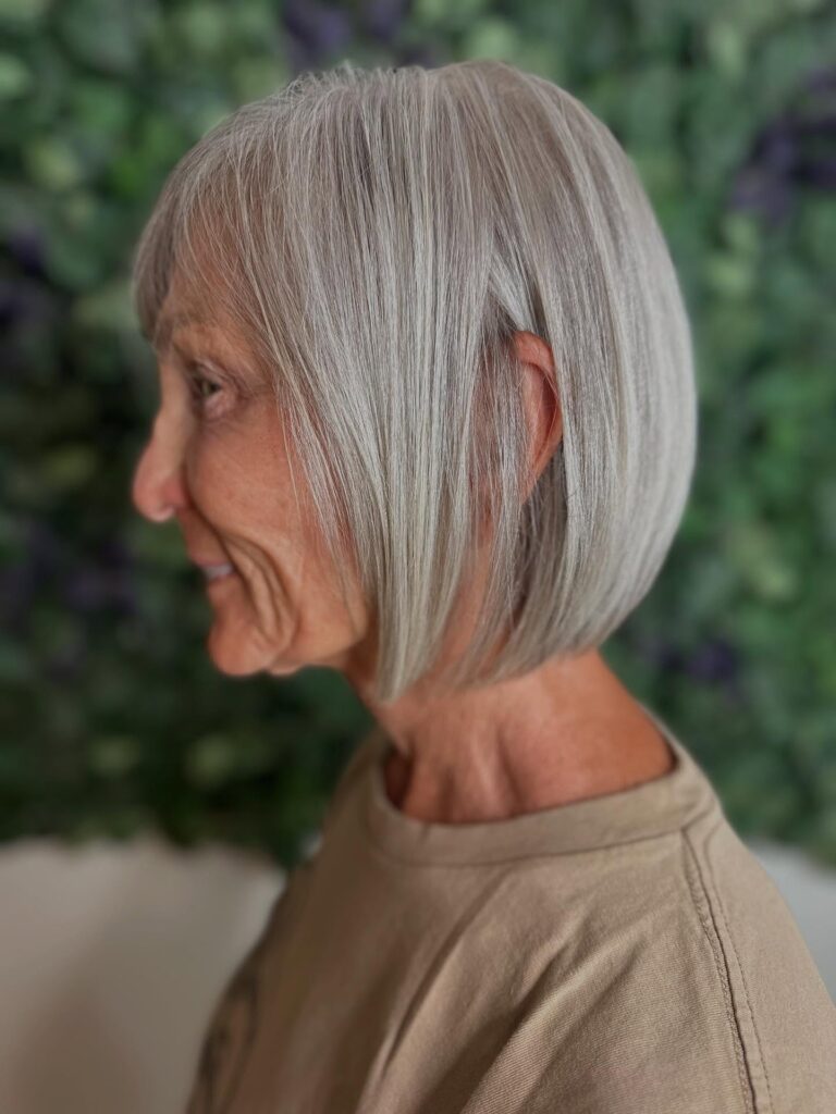 A woman with fine hair wears a sleek silver chin length bob with a rounded back and smooth finish.