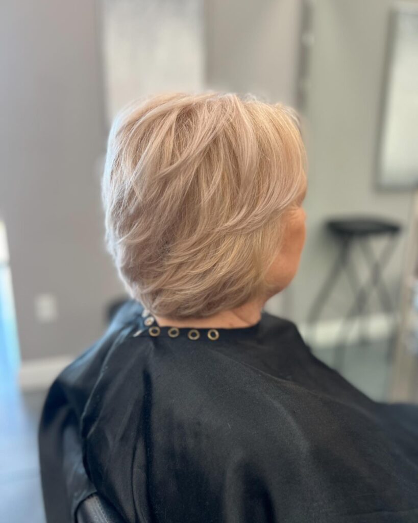 A woman with thin fine hair wears a champagne blonde feathered bob with short textured layers swept back for volume.