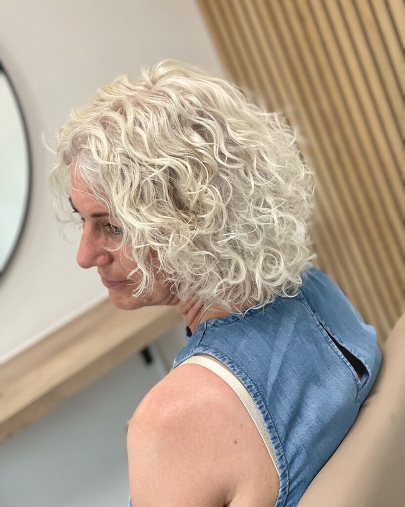 Chin-length curly bob with soft gray curls and a lightly stacked, textured shape.