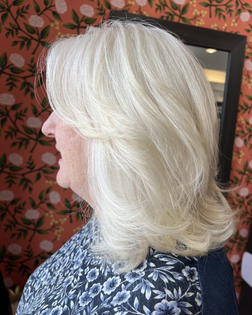 A woman with bright platinum white shoulder length hair styled in soft layers with the ends curled upward.