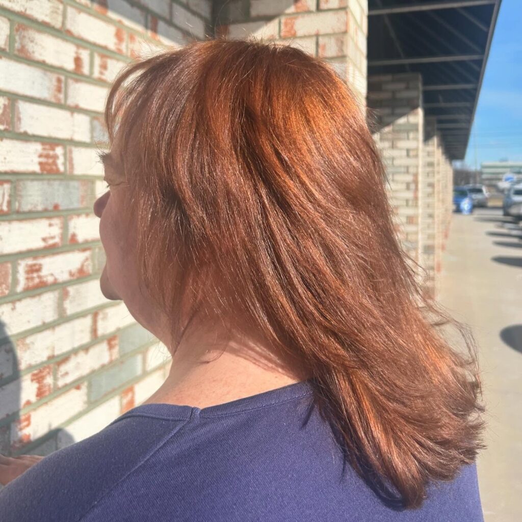 A woman with a round face wears a chin length caramel brown bob with straight hair and ends tucked inward.