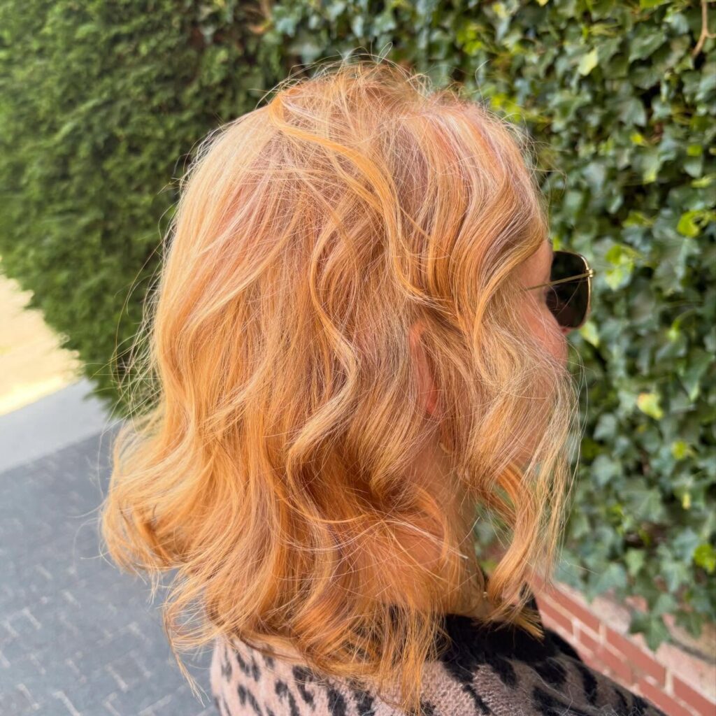 A woman with a shoulder length wavy bob in a bright strawberry blonde and copper hair color.