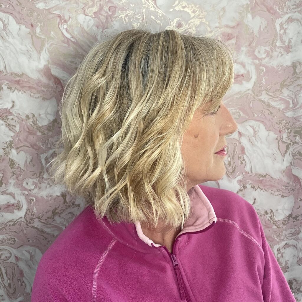 A woman with medium length creamy blonde hair styled in soft and large sculpted waves.