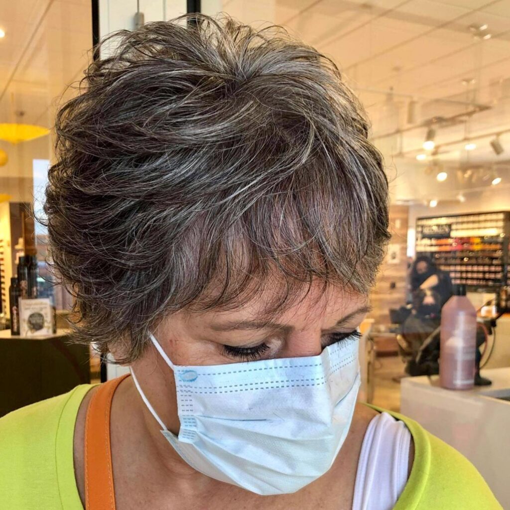 A woman with a short wispy pixie cut in smokey grey and silver featuring feathered layers and a light fringe.