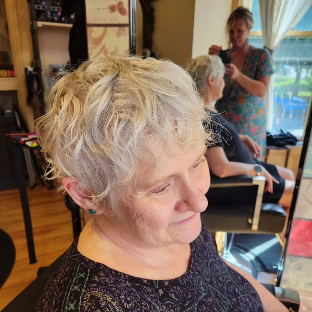 A woman with a short silver white textured crop featuring soft wavy layers and a tapered back.