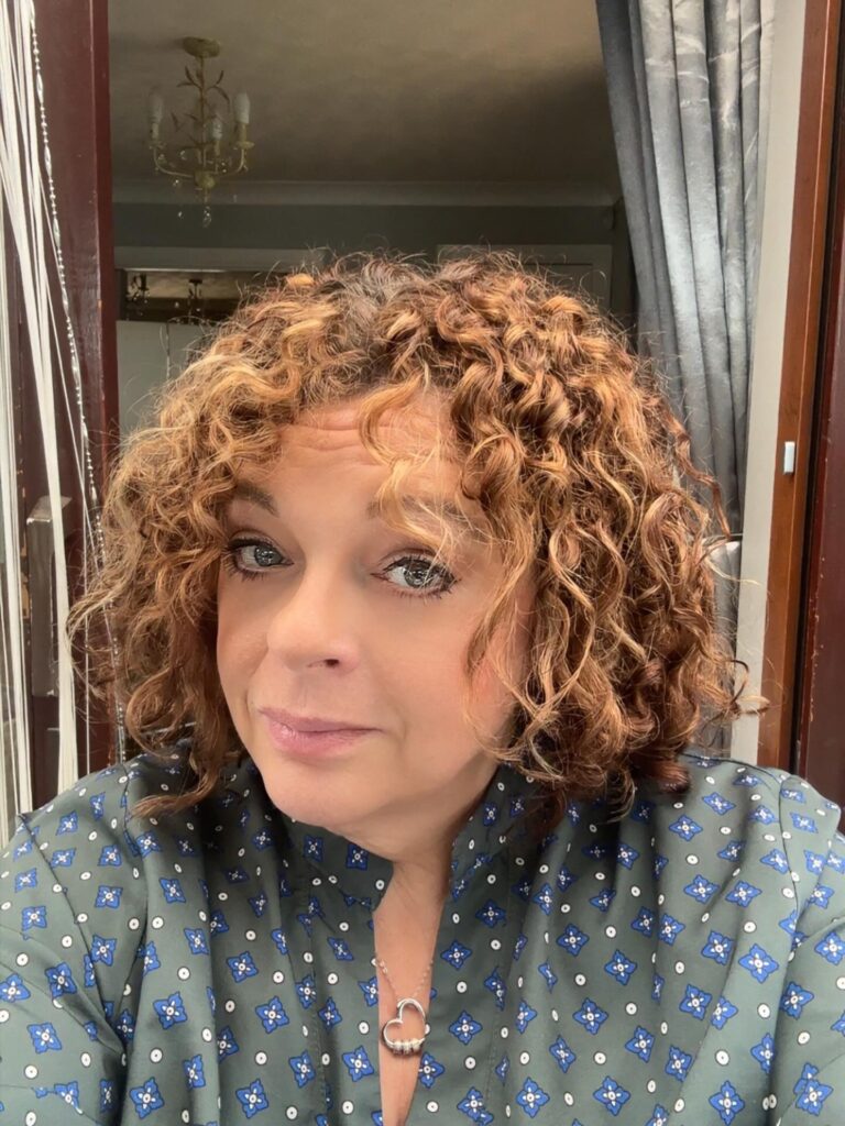 A woman with a chin length bob featuring tight golden caramel corkscrew curls and dark roots.