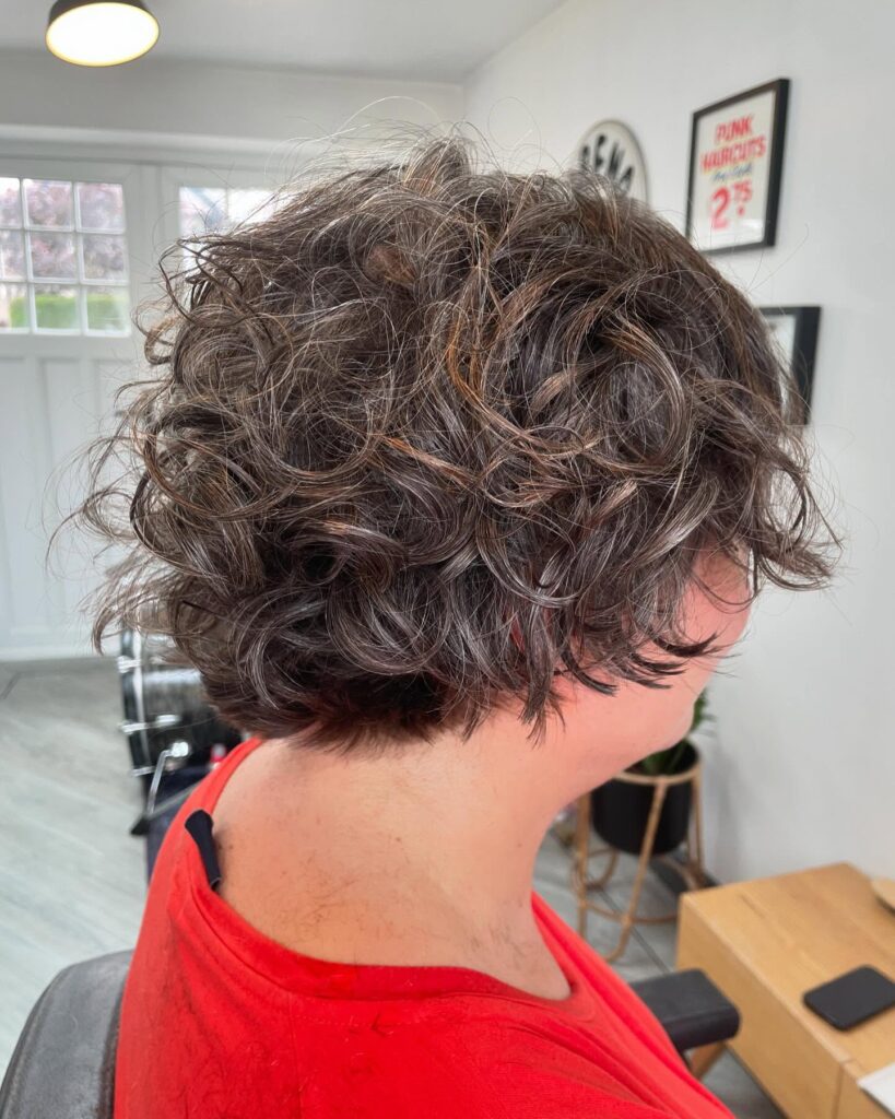 A woman with a chin length dark brunette bob featuring messy springy curls and layers.