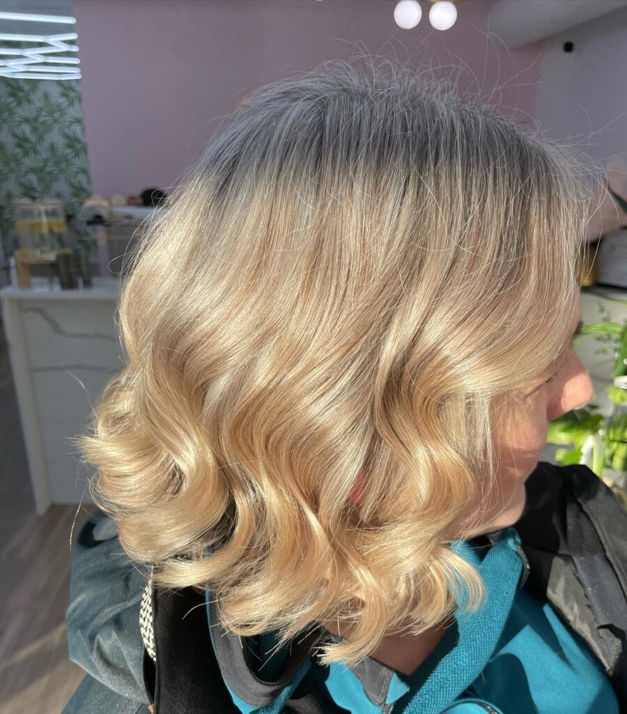 A woman with a shoulder length bright white lob featuring soft voluminous waves and a side part.