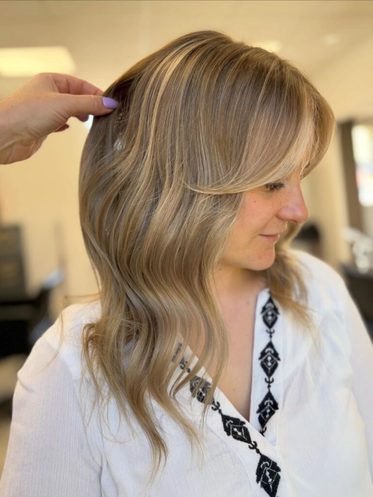 A woman with medium length ash blonde hair featuring soft waves and face framing layers.