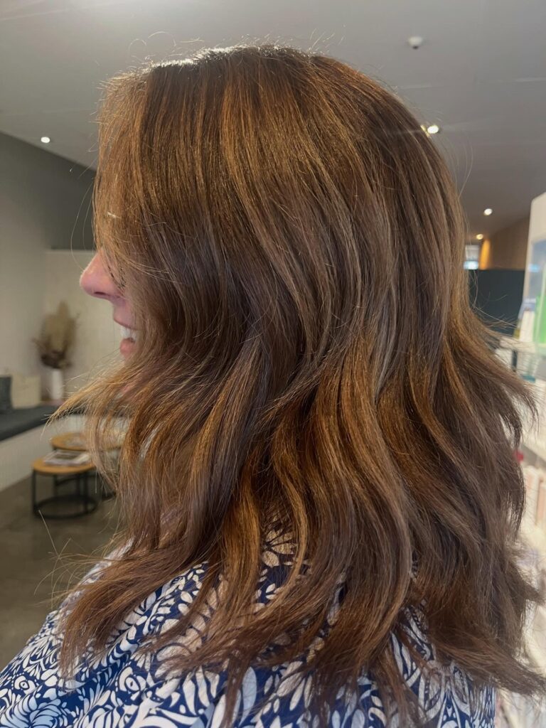 A woman with shoulder length wavy hair in a warm chocolate brown color with subtle caramel highlights.