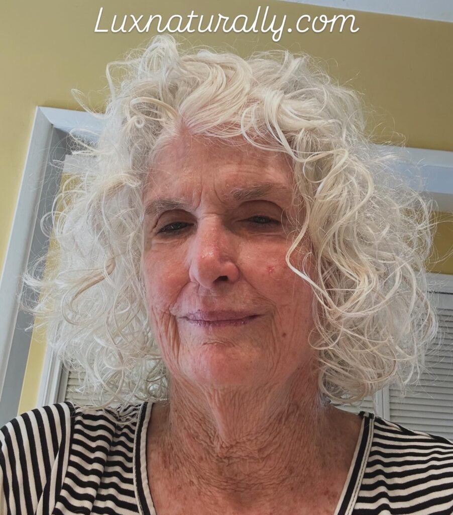 A woman with shoulder length natural white hair featuring tight bouncy curls and spirals.