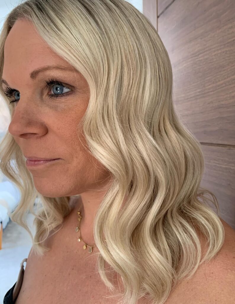 A woman with medium length icy blonde hair styled in deep polished waves.
