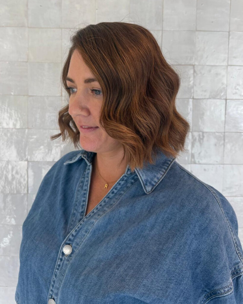 A woman with a blunt chin length bob in a rich auburn color styled with soft sculpted waves.