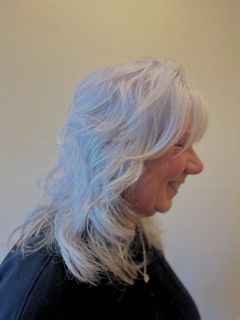 A woman with medium length platinum white hair featuring a shaggy layered cut and wispy bangs.