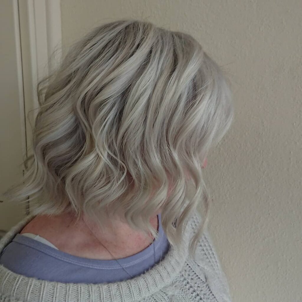 A woman with shoulder length snow white hair featuring voluminous wild ringlets and soft layers.