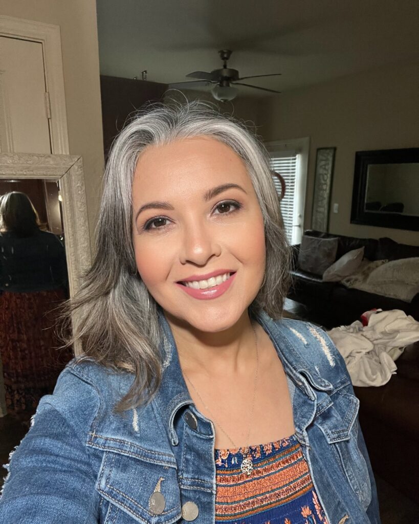 A smiling woman with shoulder-length salt-and-pepper hair styled in soft outward layers.