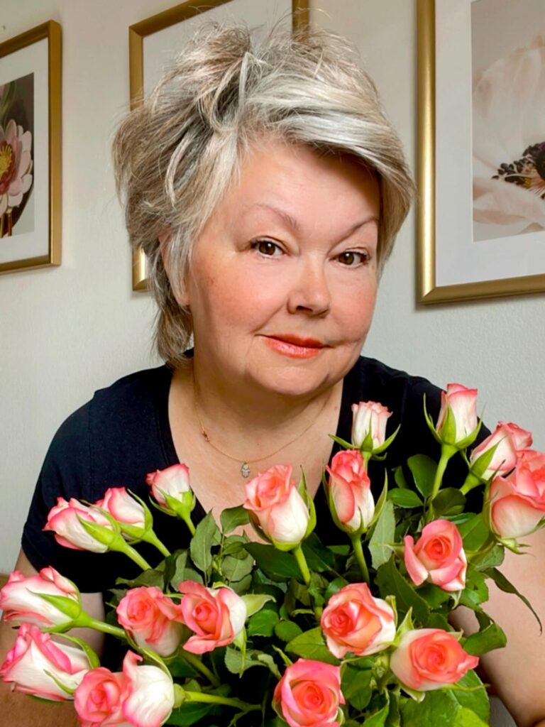 A woman over 50 with a voluminous ash blonde pixie cut featuring textured layers swept to the side.