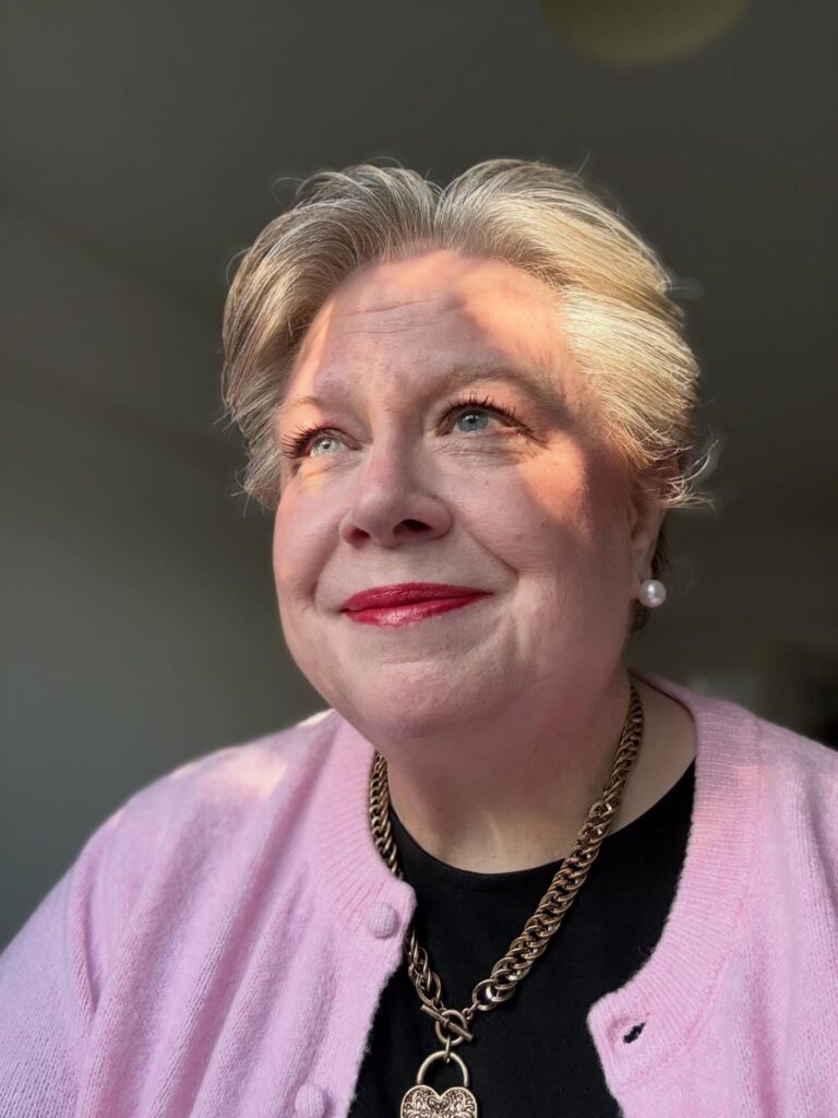 A smiling woman over 50 with short swept-back silver hair and voluminous waves at the crown.