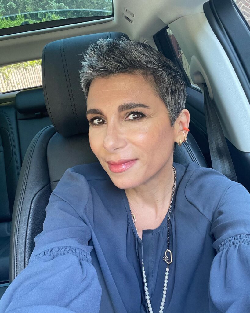 A woman with a very short, spiky pixie cut in a salt-and-pepper grey shade.