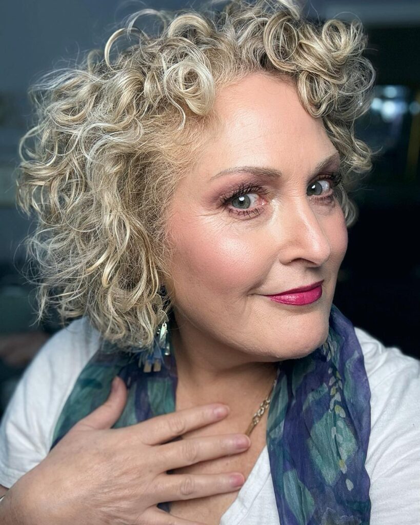 A woman with tight, voluminous champagne blonde curls in a shoulder-length bob.