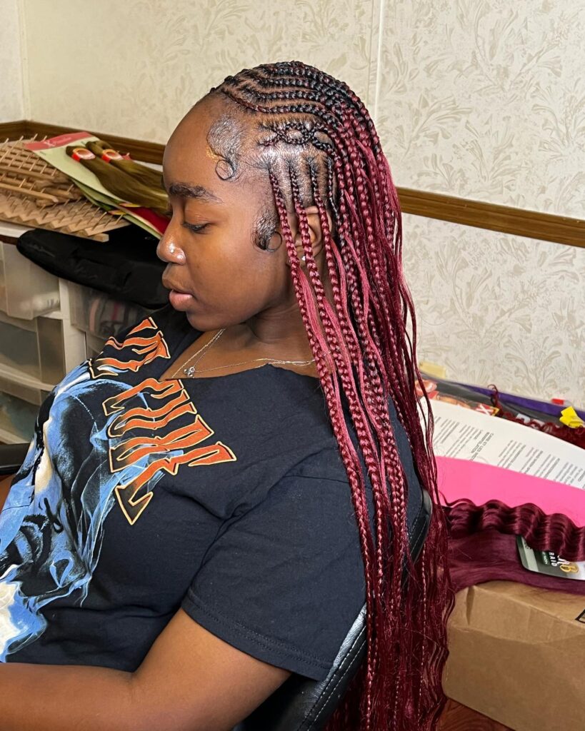 Burgundy braids with a side part and curved cornrow design flowing into long braids.