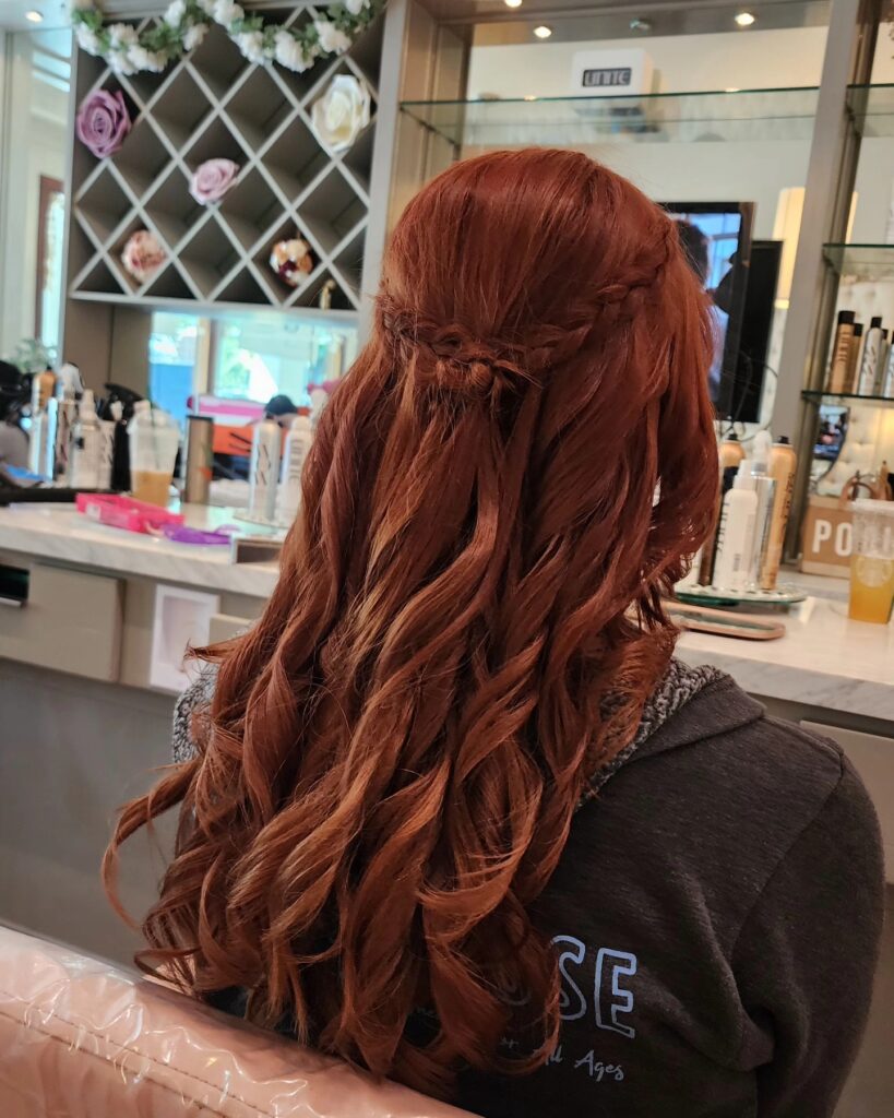 Soft auburn wavy hair styled in a half up look with a small braid detail at the back.