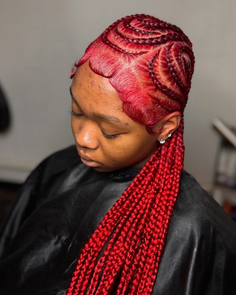 Bright red braids with sculpted swirl patterns and sleek styled edges.