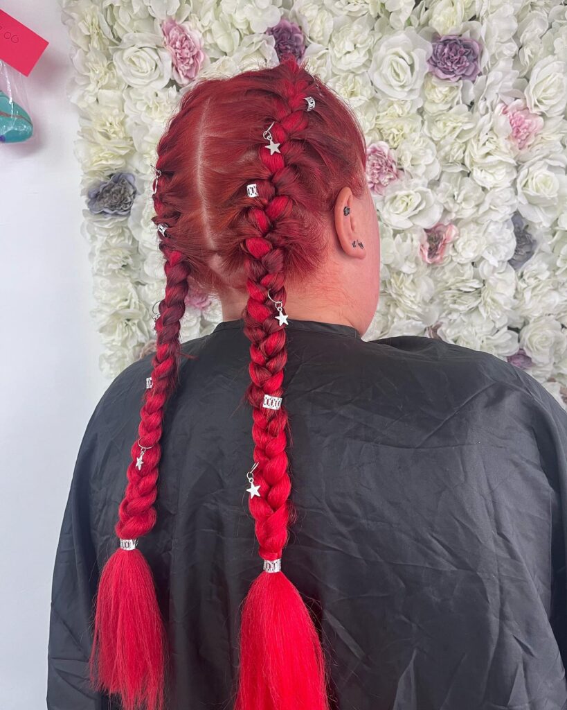 Bright red hair styled into two thick braids with decorative clips along the length.