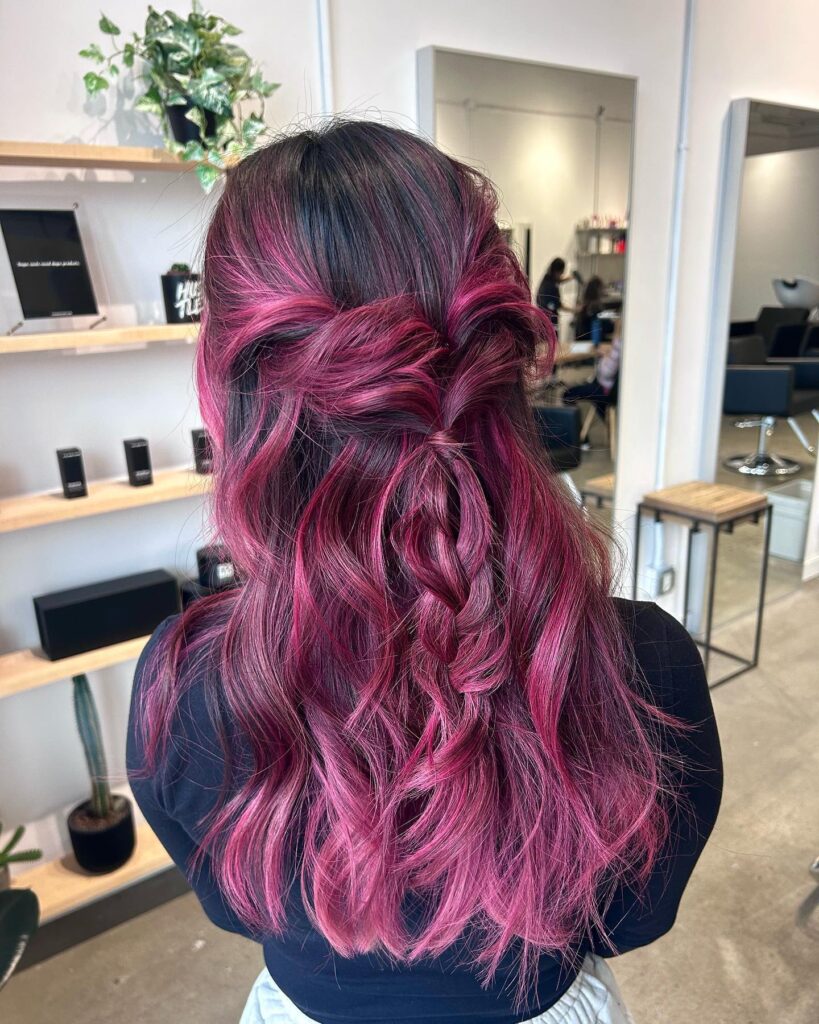 Half up hairstyle with a loose braid and wavy magenta toned hair over dark roots.