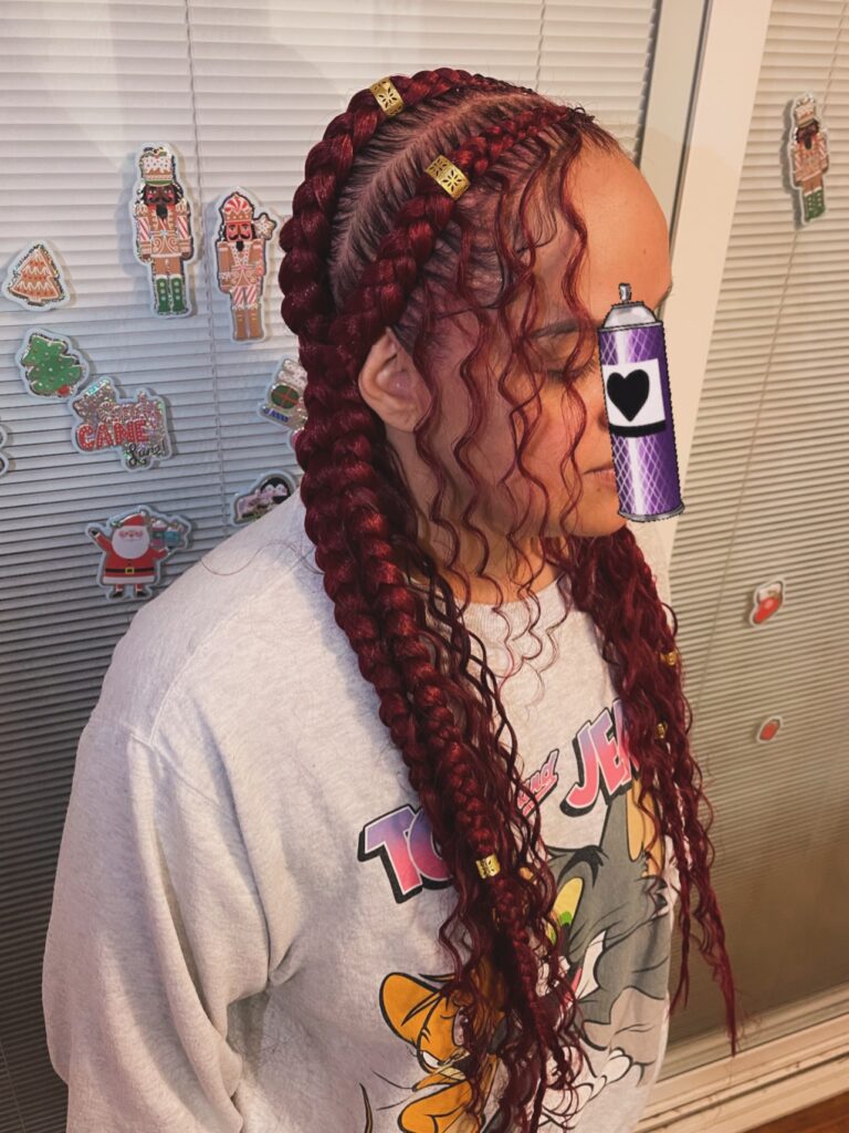 Thick deep red braids with loose curly strands framing the face and gold accents.