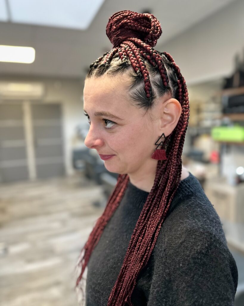 Burgundy braids styled in a high top knot with long braids hanging down.